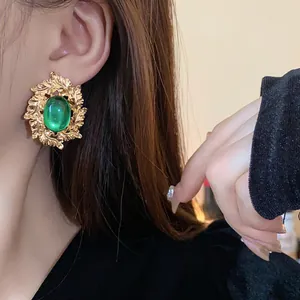 Close-up of vintage gold leaf earrings with a large green oval gemstone on a model's ear