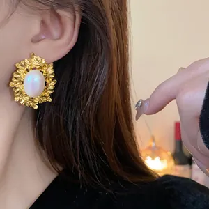 Close-up of a vintage leaf-patterned gold earring with an oval pearl on a model's ear.