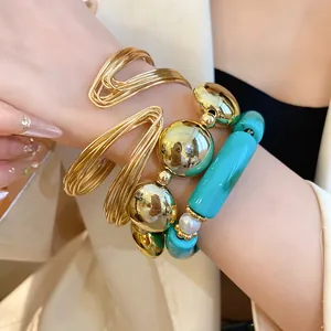 Close-up view of a golden metal wire bangle and turquoise acrylic bead bracelet set