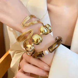 Detail view of stacked gold bangles and acrylic pearl bracelet on a model's wrist