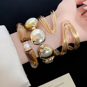 Detailed view of layered gold bangles and acrylic pearl beaded bracelets on wrist