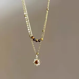 Detaillierte Nahaufnahme einer Vintage Goldkette mit Sonnenanhänger und echten Tigerauge Perlen