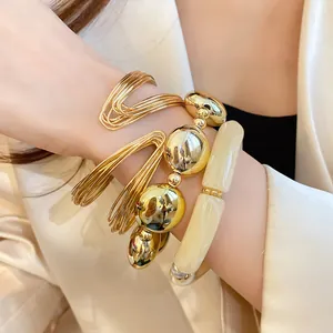 Detail of stacked gold bangles and acrylic bead bracelets on a woman's wrist.