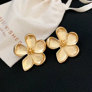 Primer plano de elegantes pendientes de flor en oro mate con una bolsa de regalo blanca