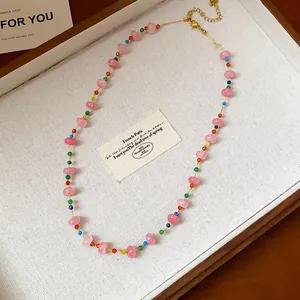 Vue détaillée d'un collier de perles en verre coloré sur un plateau texturé blanc