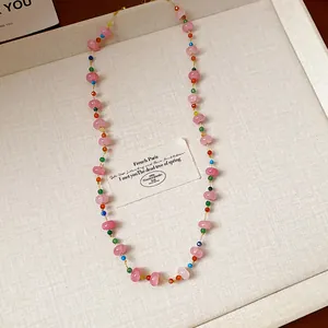 Gros plan d'un collier de perles de verre colorées avec fil d'acier sur plateau beige.