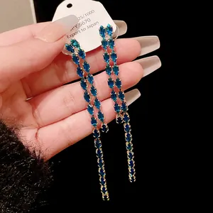 Dettaglio di orecchini a nappa lunga con zirconi blu scintillanti e perni in argento