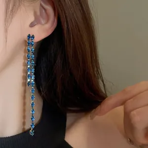 Primo piano di lunghi orecchini a nappa con zirconi blu indossati con eleganza