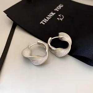 Close-up of silver twisted hoop earrings with a textured braided design