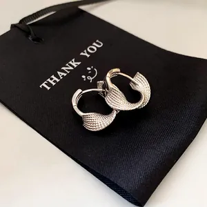 Macro view of minimalist silver twisted hoop earrings on a textured black gift pouch