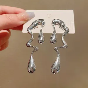Primo piano di orecchini a goccia in metallo liquido irregolare color argento.