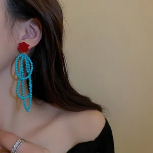 Nahaufnahme von Boho-Ohrringen mit roten Blumen und langen blauen Perlenquasten