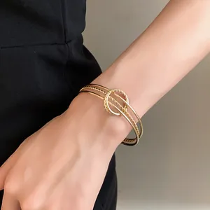 Dettaglio di un bracciale a fascia aperta in oro intrecciato irregolare minimalista