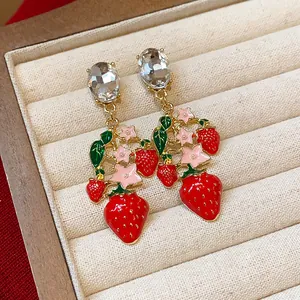 Nahaufnahme eleganter roter Erdbeer-Ohrringe mit funkelnden Zirkonen und rosa Blüten