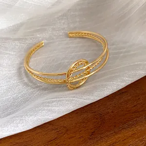 Primo piano di un bracciale rigido dorato con nodo intrecciato su fondo in tessuto.