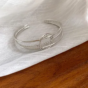 Primo piano di un bracciale rigido argento minimalista con raffinati dettagli in corda intrecciata