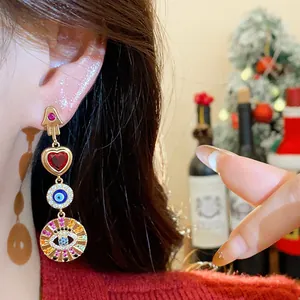 Nahaufnahme von luxuriösen langen Ohrringen mit Hamsa-Hand, rotem Herz und bösem Blick Motiv.