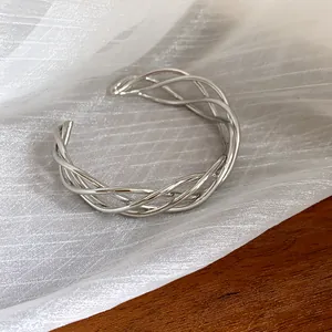 Dettaglio macro di un bracciale a fascia ritorto in argento su tessuto bianco.