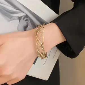 Vista dettagliata di un bracciale a fascia aperta dorato intrecciato su polso femminile.