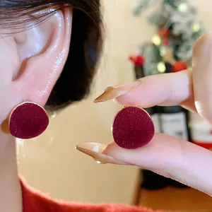 Close-up of elegant red flocked stud earrings with gold trim on ear for festive look