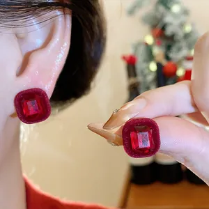 Close-up detail of red flocked square stud earrings featuring a radiant faceted gemstone