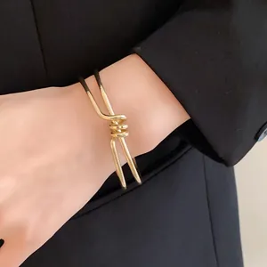 Primo piano di un bracciale rigido dorato ritorto irregolare indossato al polso.