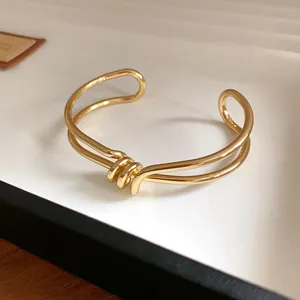Primo piano di un bracciale a polsino dorato minimalista con design a nodo intrecciato