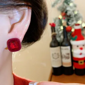 Close-up detail of a red flocked geometric ear stud with a faceted ruby-like stone.