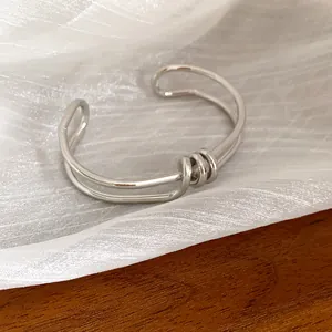 Primo piano di un bracciale rigido argento ritorto minimalista su tessuto bianco