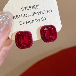 Close-up detail of red velvet flocked stud earrings with large square-cut red gemstone