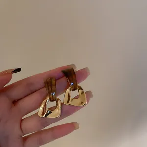 Geometric tortoiseshell and gold drop earrings held by hand for detailed close-up view