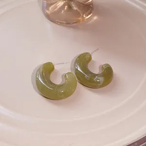 Macro view of olive green marbled resin C-shaped hoop earrings with silver posts