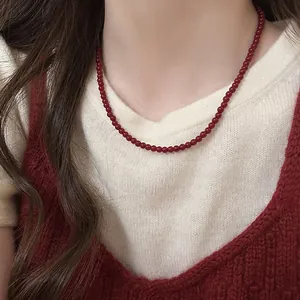 Detailed close-up view of an elegant red bead necklace worn over a white knit sweater.