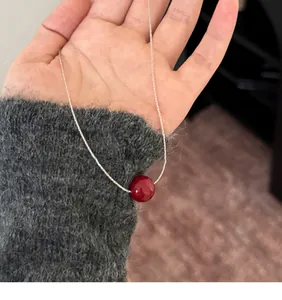 Close-up of a vibrant red bead pendant on a silver chain against a grey sweater sleeve