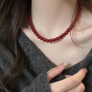 Close-up of deep red bead necklace worn over a grey V-neck sweater, autumn jewelry style