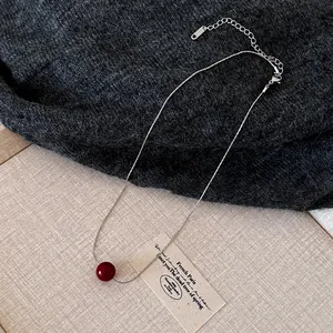 Close-up of a silver chain necklace with a vibrant red bead pendant on a sweater