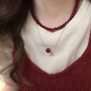 Close-up of a layered necklace with red beads and a pendant on a silver chain.