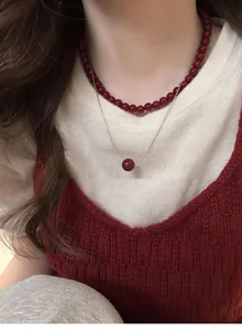 Close-up of Ancora red bead pendant necklace layered over a cozy winter sweater
