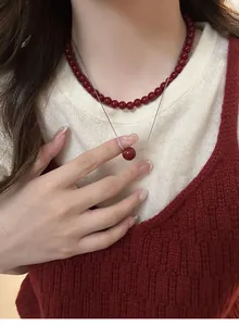 Close-up of elegant red lucky bead pendant necklace worn over a white knit sweater.