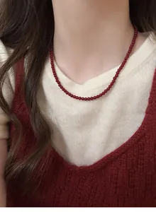 Detailed view of a retro red beaded necklace worn over a cozy cream knitted sweater
