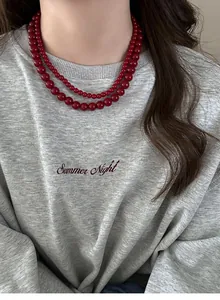Detailed view of an elegant double-layered dark red bead necklace worn on a gray sweatshirt