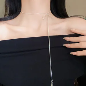 Detailed close-up of minimalist silver bow tassel necklace on female model collarbone