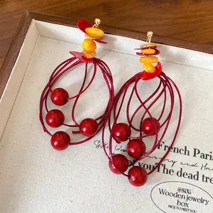 Detailed view of red beaded tassel earrings with multi-strand loops and orange chips