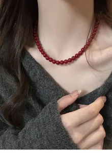 Close-up of elegant red beaded necklace worn over a soft grey knitted sweater