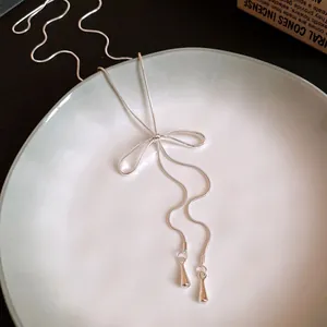 Close-up detail of a minimalist silver bow tassel necklace with teardrop pendants