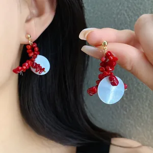 Detailed close-up of elegant red beaded tassel earrings with white shell detail on model