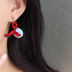 Close-up of elegant red acrylic beaded earrings with white geometric shell detail