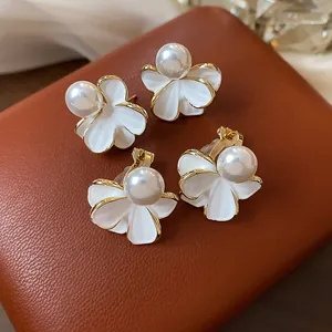Dettaglio di eleganti orecchini a fiore bianchi con bordi dorati e perle centrali.