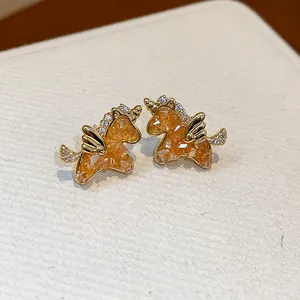 Primer plano de pendientes de unicornio dorados con incrustaciones de cristal naranja