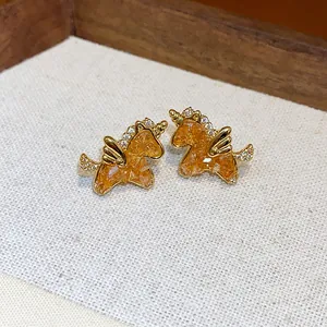 Primer plano de elegantes pendientes de unicornio dorados con resina naranja y circonitas